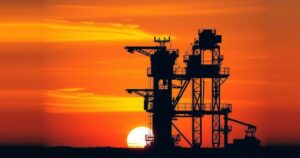 Oil rig silhouette against sunset with a warm orange and yellow color scheme, symbolizing energy exploration.