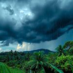 Cloudy skies with dark storm clouds forming and heavy rain falling over lush tropical landscape in the Philippines.